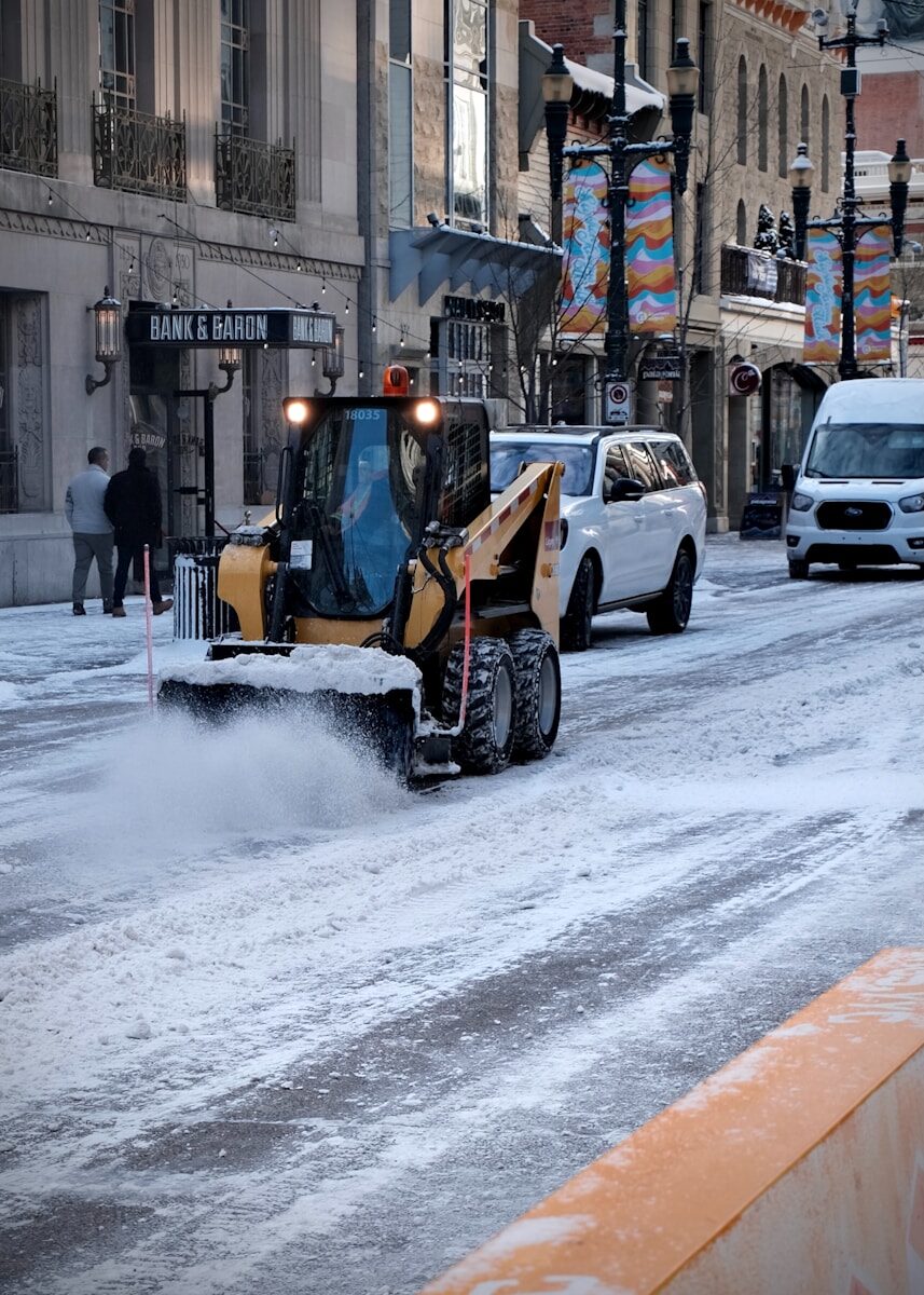 Skid steer loader plowing snow on a city street.